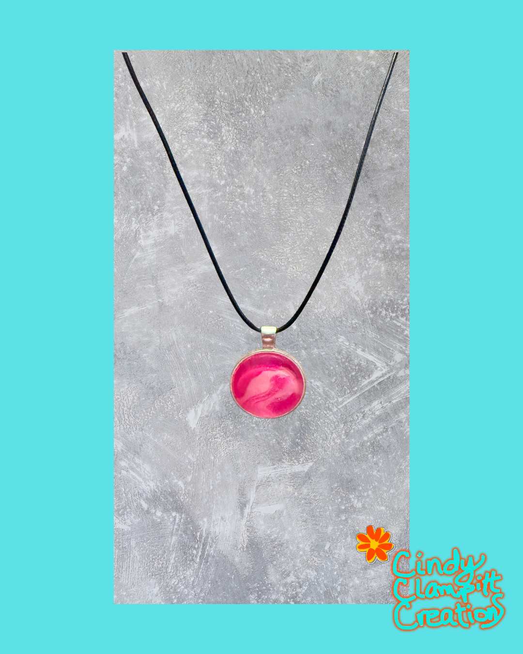 A pink marbled pendant necklace on a black cord, displayed against a textured gray background with a turquoise border and a 'Cindy's Creative' logo in the bottom right corner.