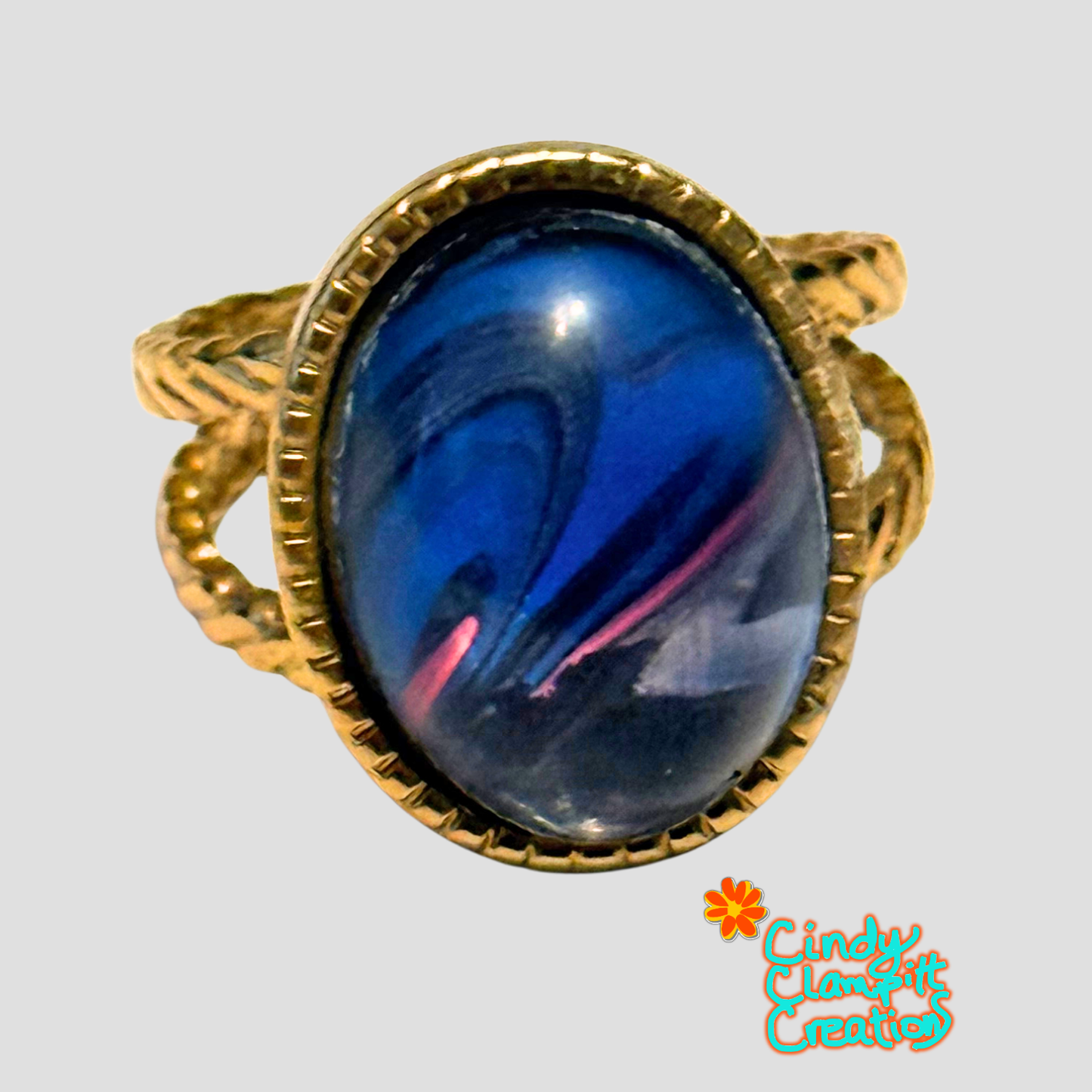 Top view of hand-painted midnight blue and magenta swirl oval glass cabochon ring on a gold twisted rope open cuff band