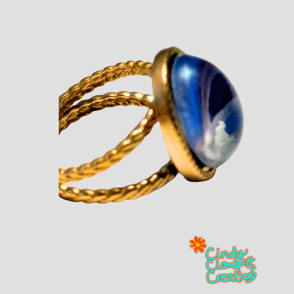 Side view of hand-painted deep blue oval glass cabochon ring on an 18K gold plated twisted rope open cuff band