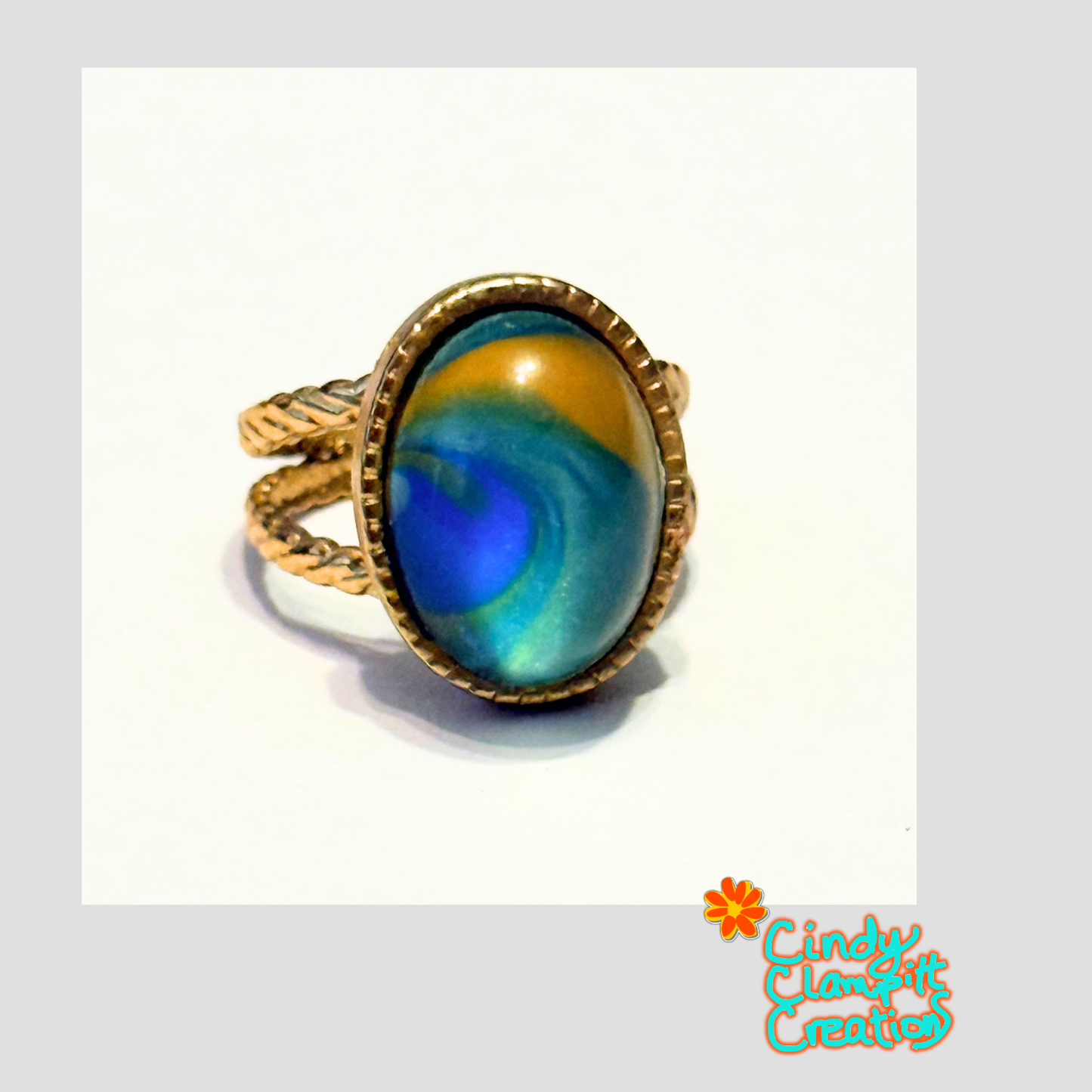 Side view of hand-painted peacock-inspired teal and gold oval glass cabochon ring on a gold twisted rope open cuff band