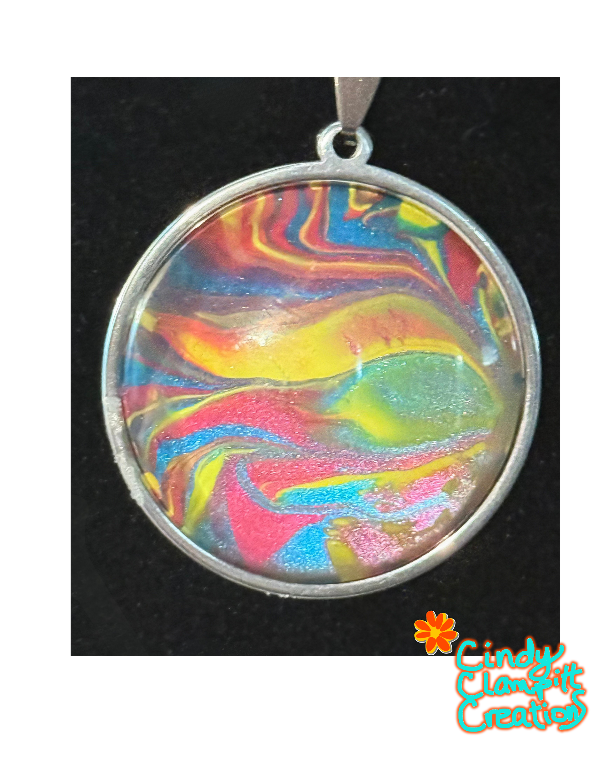 A round silver pendant with a colorful marbled resin design featuring swirls of yellow, pink, blue, and green, set against a black background with a 'Cindy's Classtic Creations' logo in the bottom right corner.